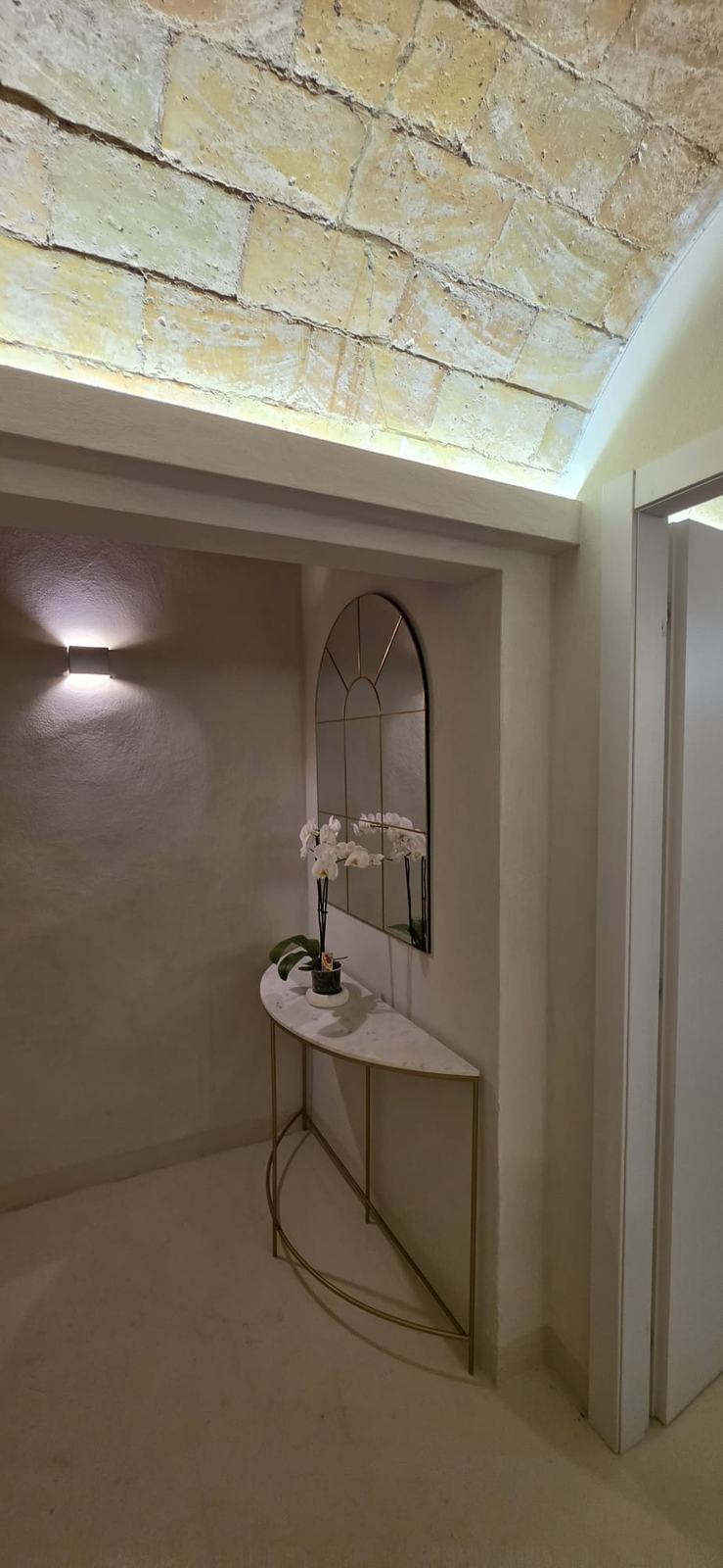 Ingresso con consolle in marmo, specchio ad arco e orchidea, sotto la volta